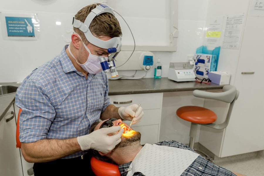 male dentist using dental equipment to look into patient's mouth